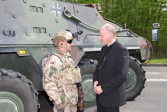 Ein Infanterist unterhält sich mit Bischof Overbeck vor dem Transportfahrzeug "Boxer". (Foto: KMS / Jörg Volpers)