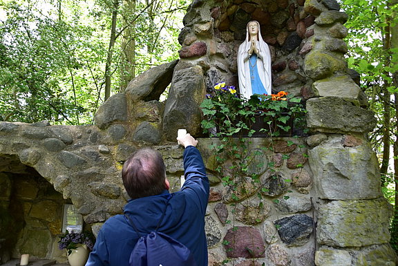 Die Lourdes-Grotte in Berlin-Lankwitz wurde von französischen Kriegsgefangenen errichtet. Ein Pilger zündet eine Kerze vor der Statue der Gottesmutter Maria an. © KS / Norbert Stäblein