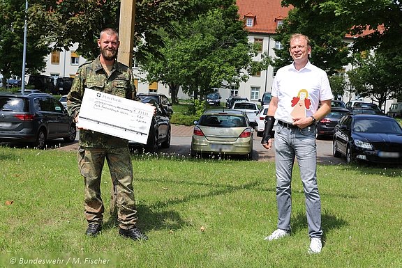 Oberstabsgefreiter Christoph Eckstein übergibt den Spendenscheck an Rainer Krotz. Dieser hält den Familienengel, das Zeichen der Stiftung, in der Hand. © Bundeswehr / Mandy Fischer 