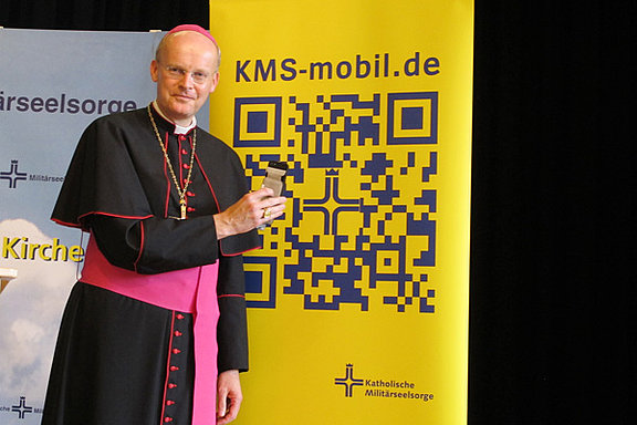 Bischof Overbeck mit Smartphone und QR-Code 
